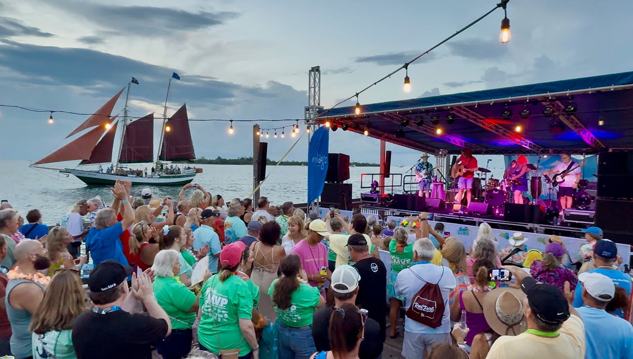 A group of people watching a band play music on a stage near the water