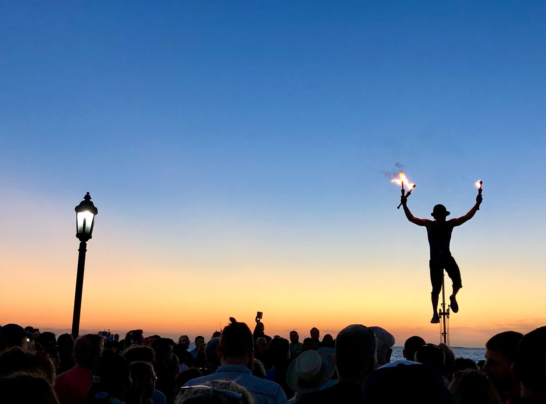A busker on a giant unicycle juggling fire sticks at night in Mallory Square