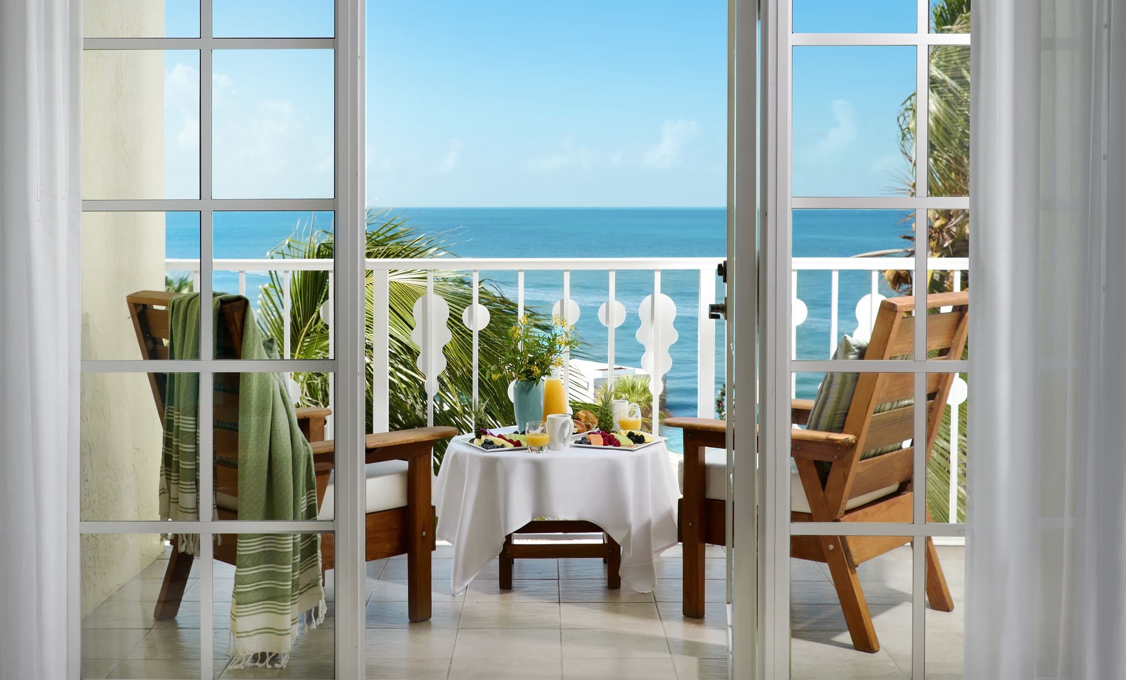 A balcony off of. 1 bedroom room at Ocean Key Resort with 2 chairs and a small table with food and drinks