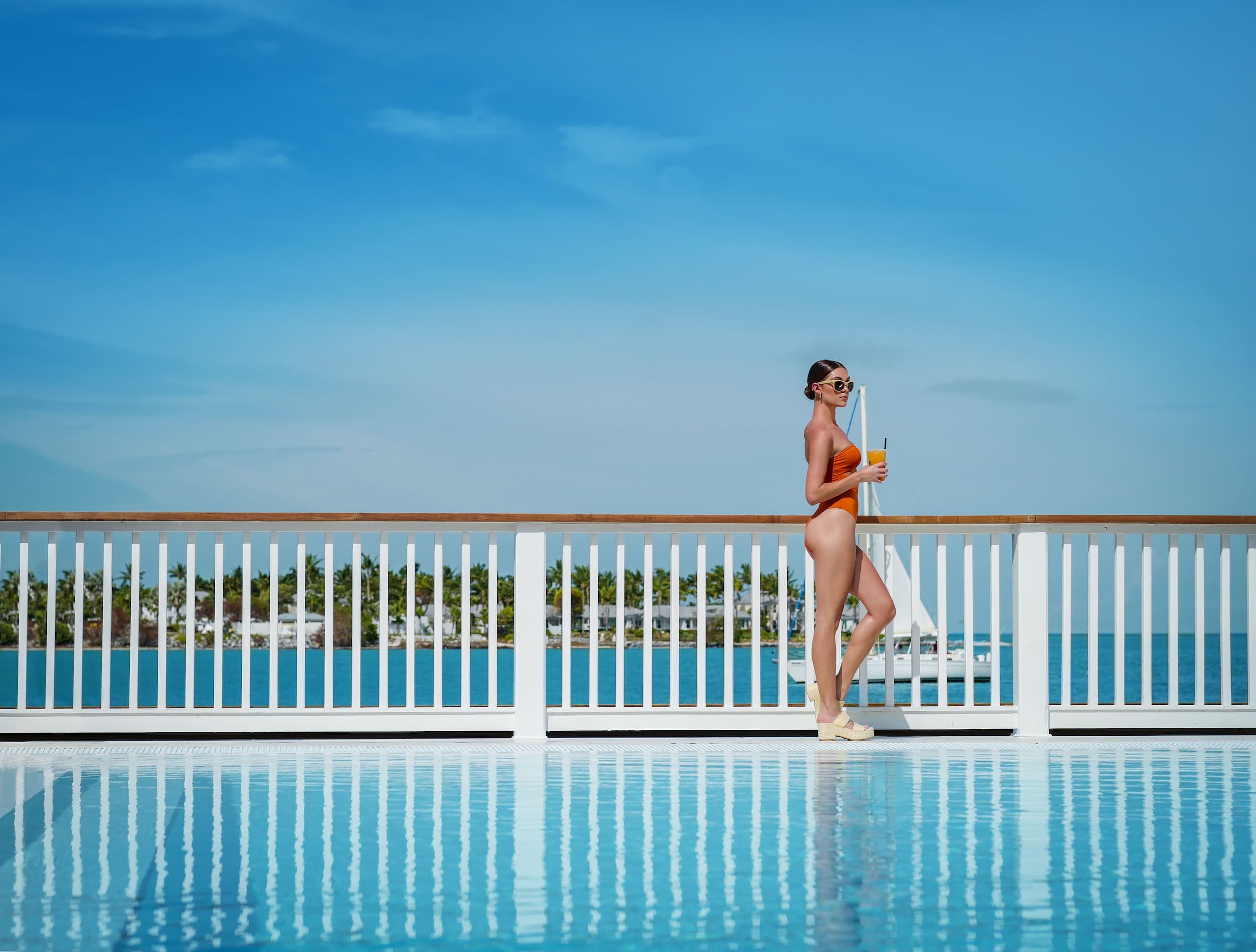 A woman standing poolside in a swimsuit with a cocktail ay Ocean Ket Resort