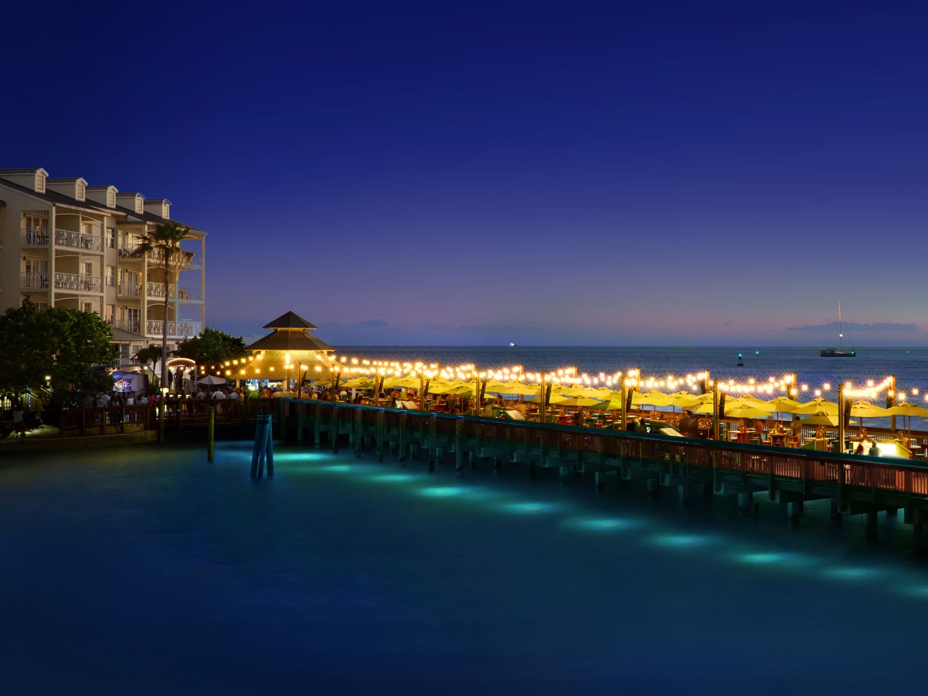 The pier at night lit up with string lights going the length of the pier at Ocean Key