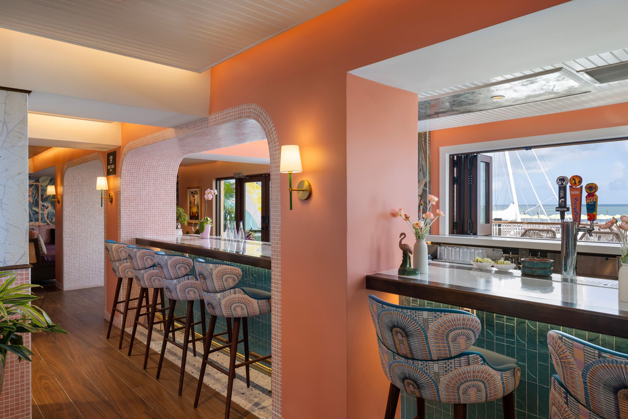 Interior bar with coral-pink walls, decorative chairs, and view toward the ocean and dining area at Ocean Key Resort, Key West