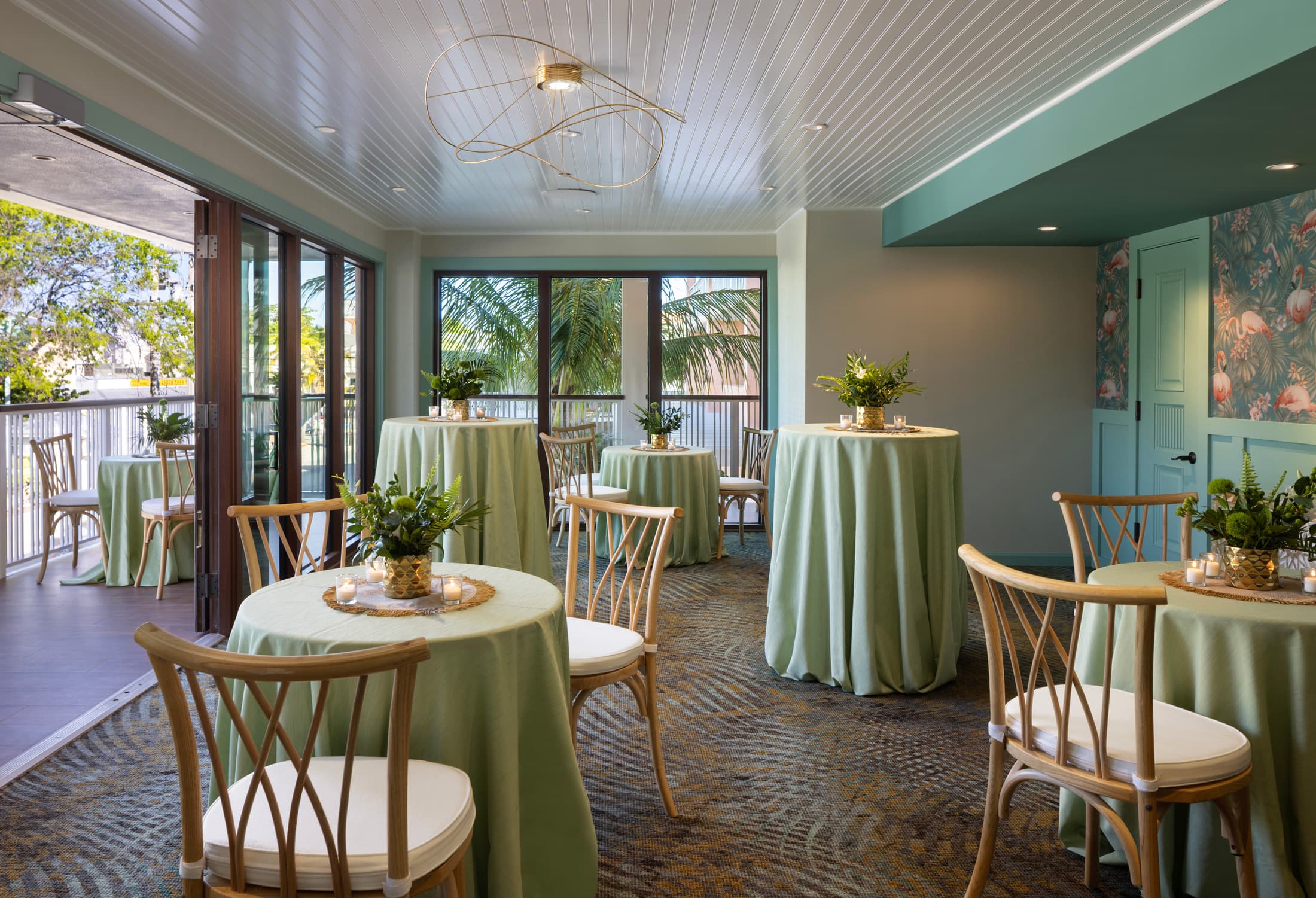Sunlit corner dining area with green chairs, round table set for two, and tall windows overlooking the garden patio at Ocean Key Resort, Key West