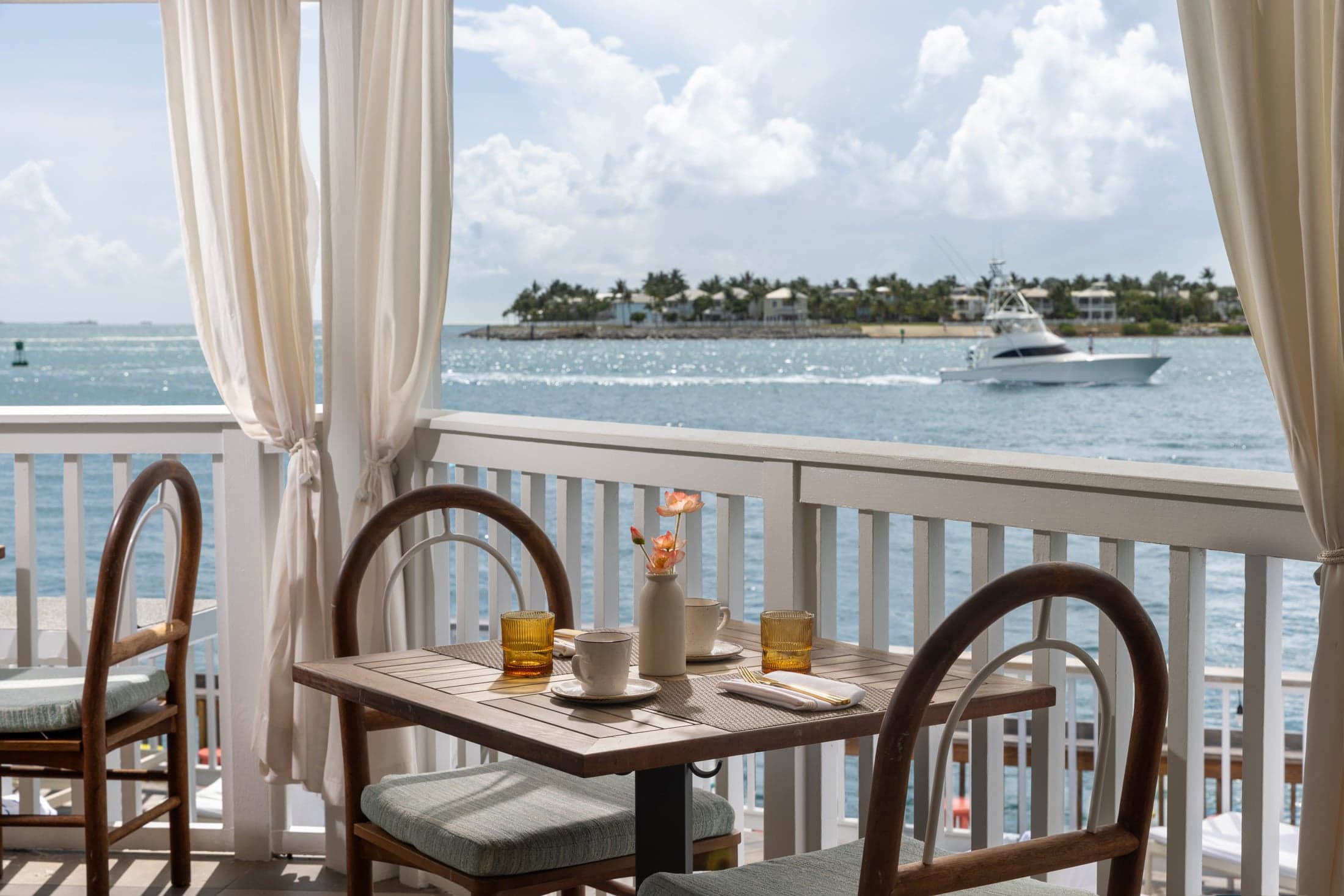 Private waterfront balcony with two chairs and a small bistro table overlooking the ocean and palm trees at Ocean Key Resort, Key West