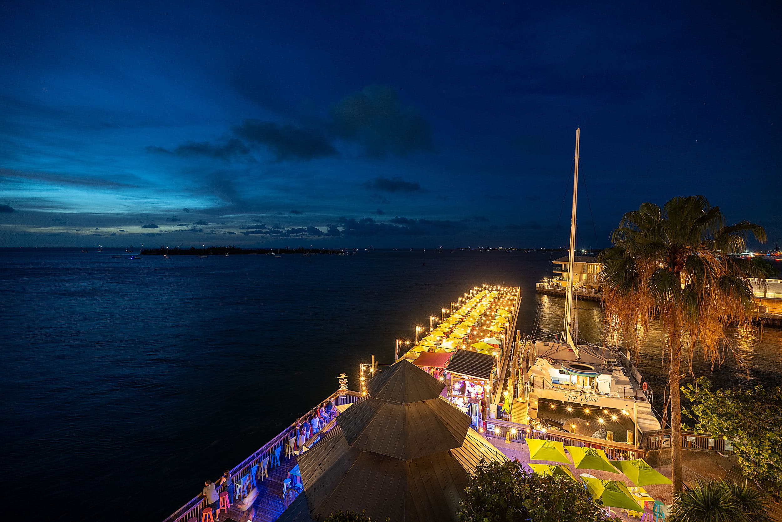 Aerial night view of the glowing Sunset Pier and harbor at Ocean Key Resort in Key West, Florida under a blue twilight sky