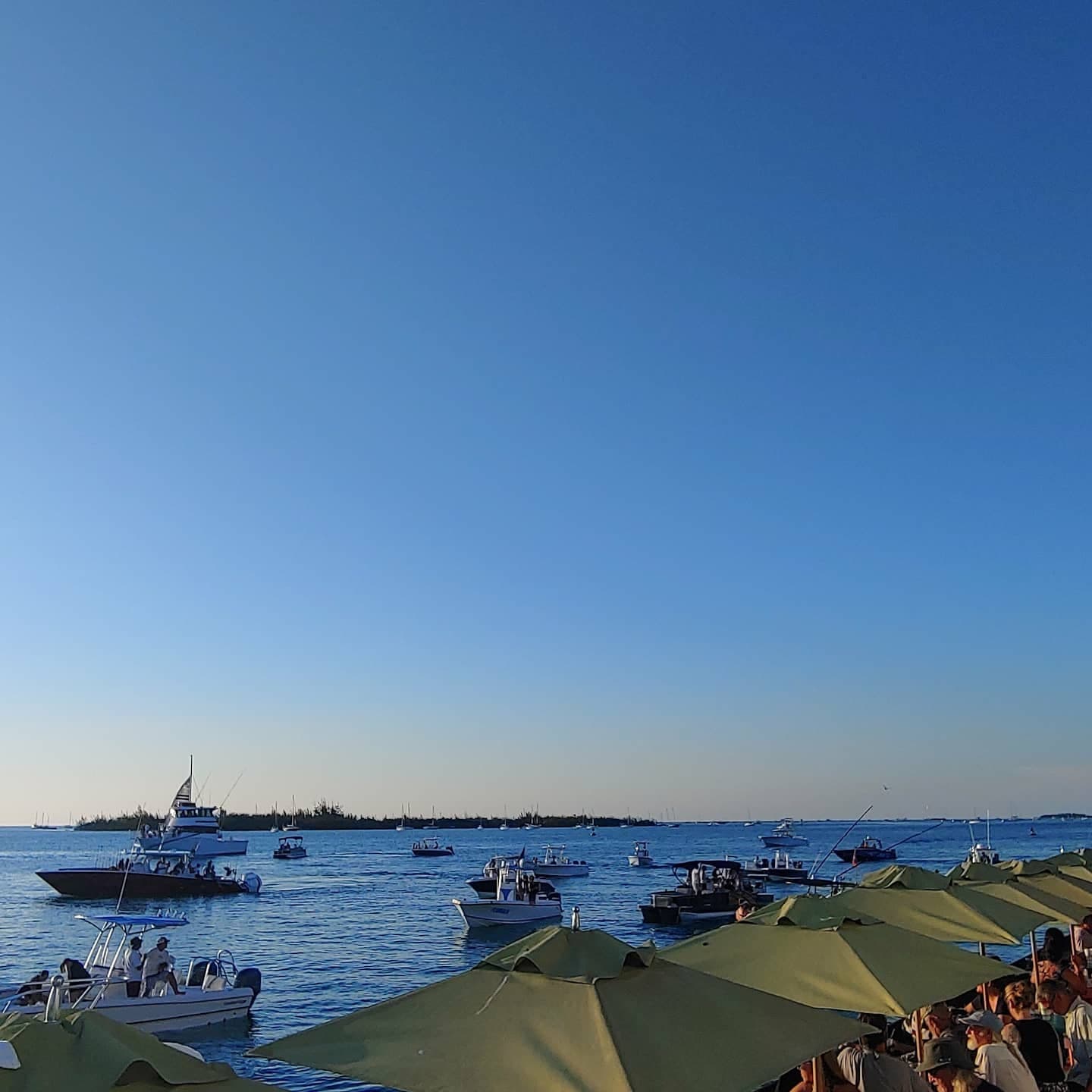Boats gathered offshore beyond green umbrellas at Sunset Pier, Ocean Key Resort in Key West, Florida