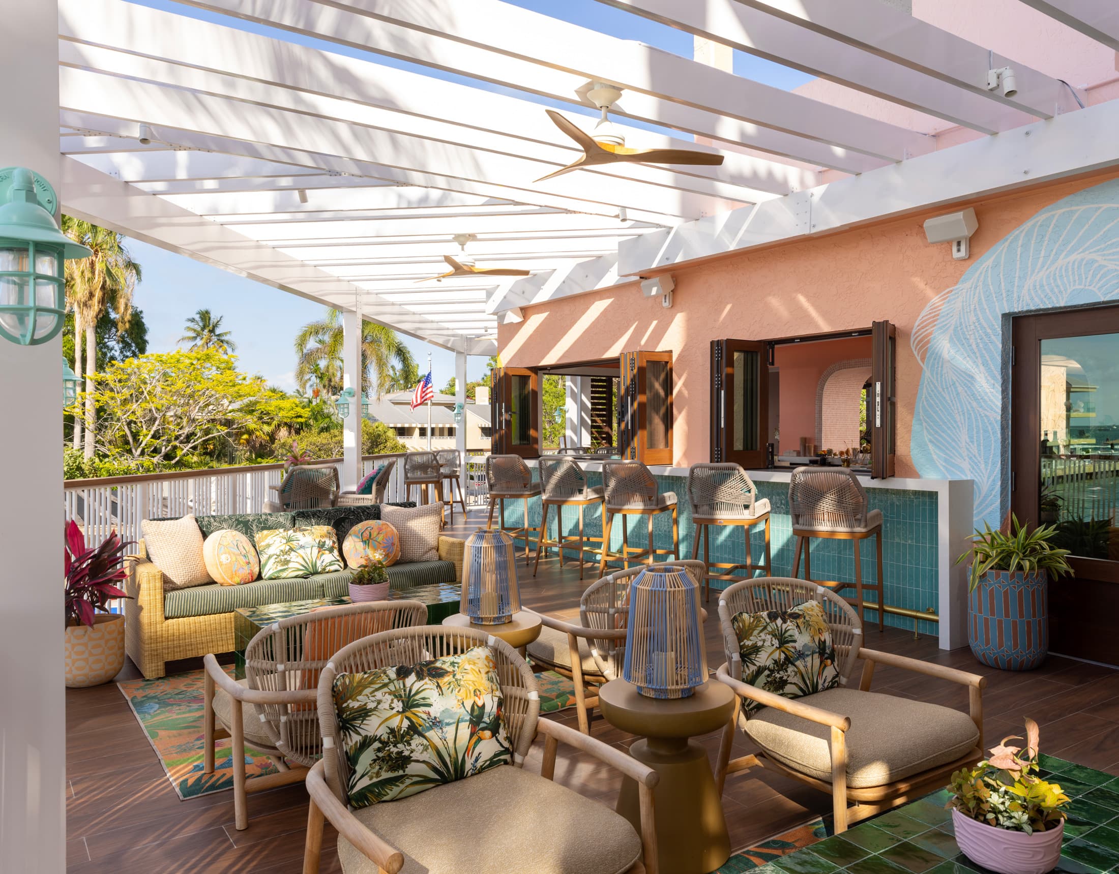 Outdoor dining terrace with wicker chairs, striped awning, tropical palm trees, and waterfront view at Sweet Bird Bar at Ocean Key Resort