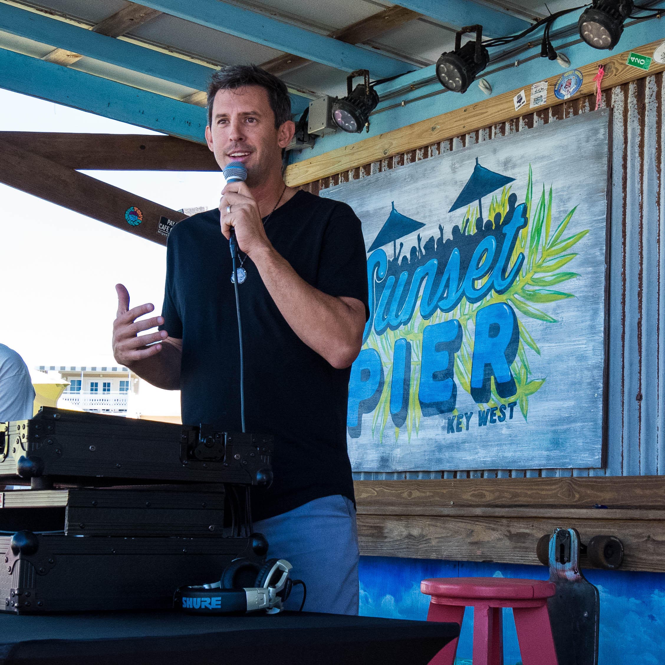 Event host speaking into a microphone beside the Sunset Pier sign at Ocean Key Resort in Key West, Florida